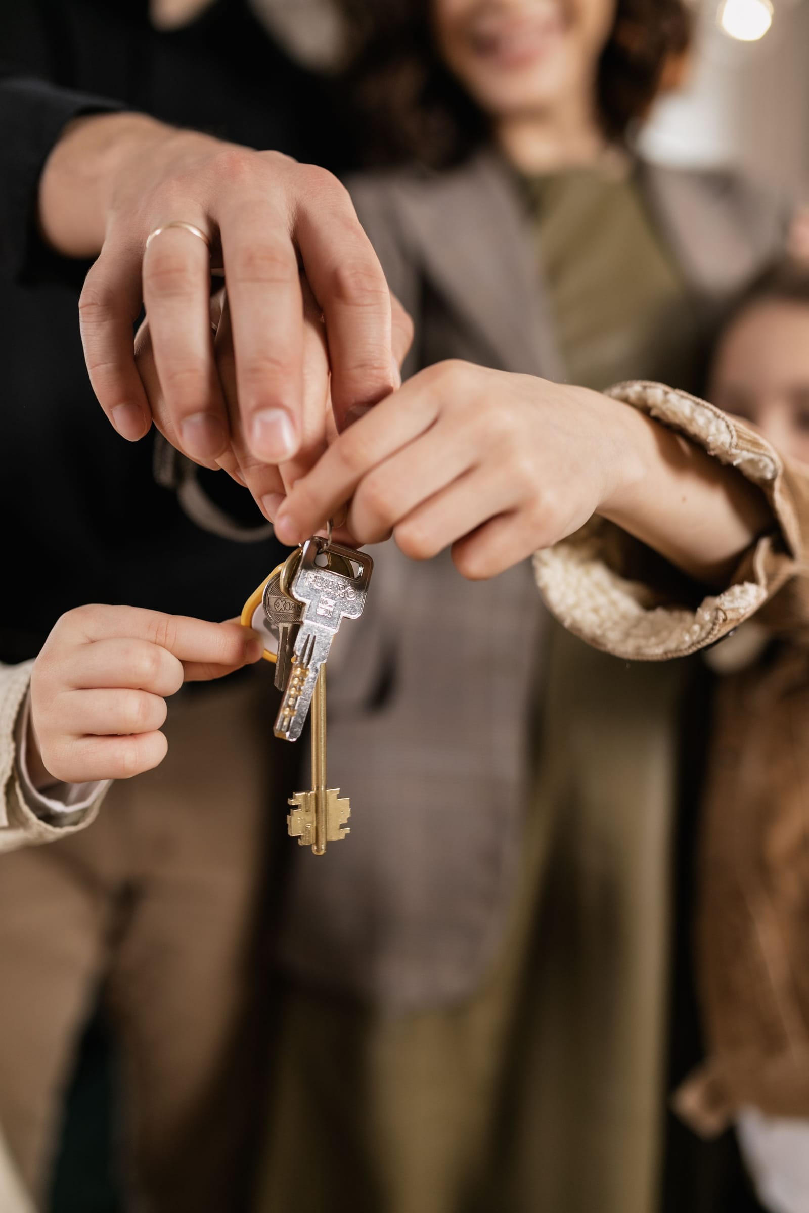 Several hands together around one set of house keys.